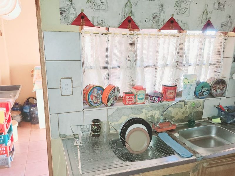 A functional kitchen area featuring a double stainless steel sink, tiled splashback, and visible wear on the wall surfaces.