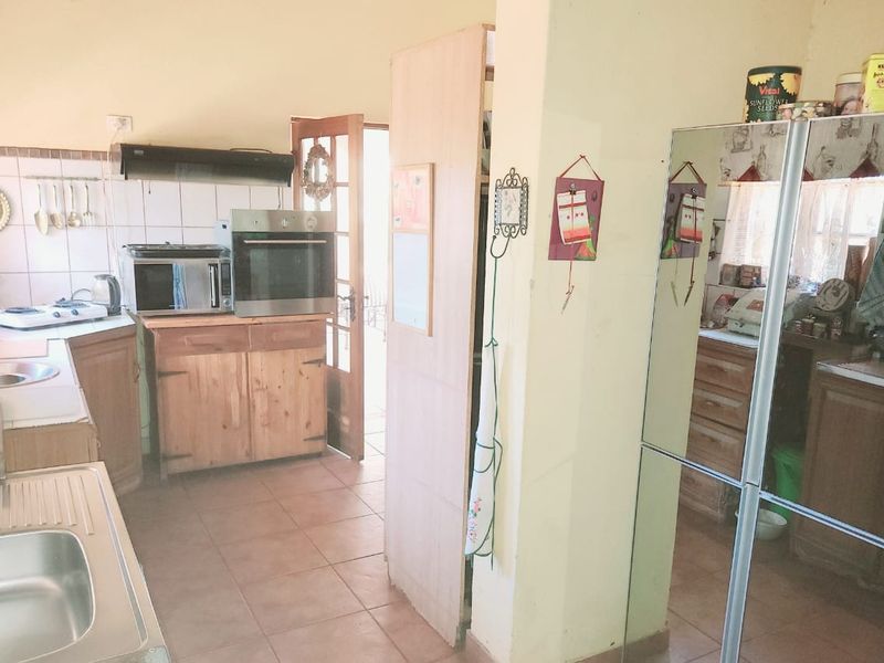 A functional kitchen area featuring wooden cabinetry, built-in oven, extractor fan, and tiled flooring with direct access to an outdoor space.