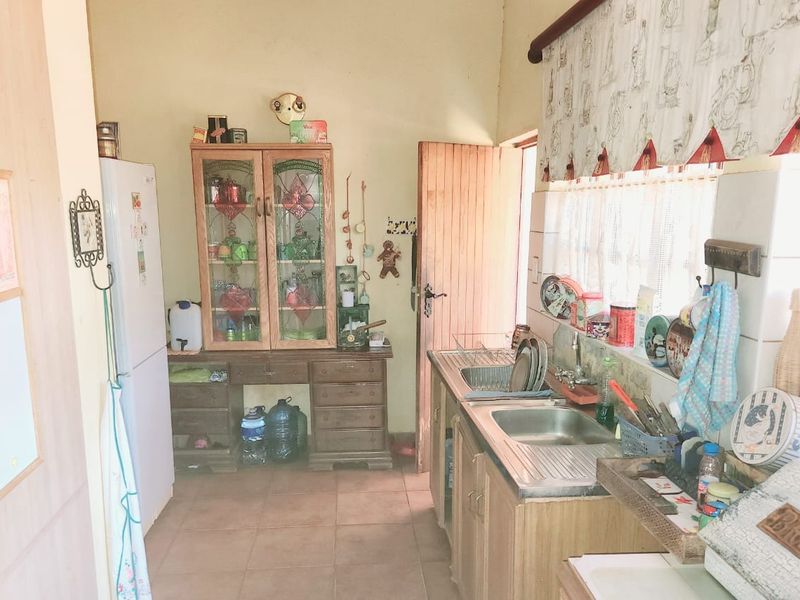 A functional farm-style kitchen featuring built-in wooden cabinetry, a stainless steel sink, and tiled flooring with direct access to the exterior.