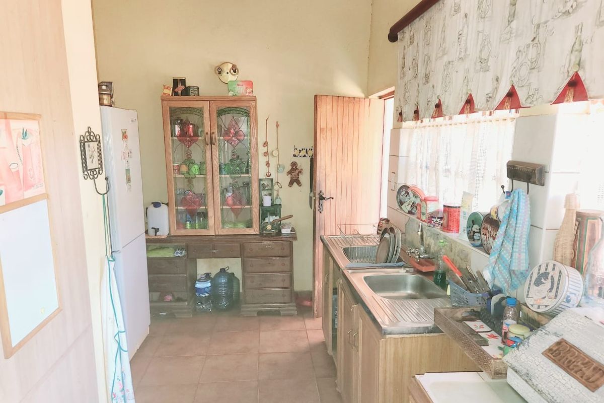 A functional farm-style kitchen featuring built-in wooden cabinetry, a stainless steel sink, and tiled flooring with direct access to the exterior.