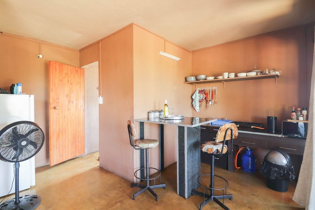 A compact kitchen area featuring a built-in breakfast bar, open shelving, and basic cabinetry, finished with painted walls and a concrete floor.