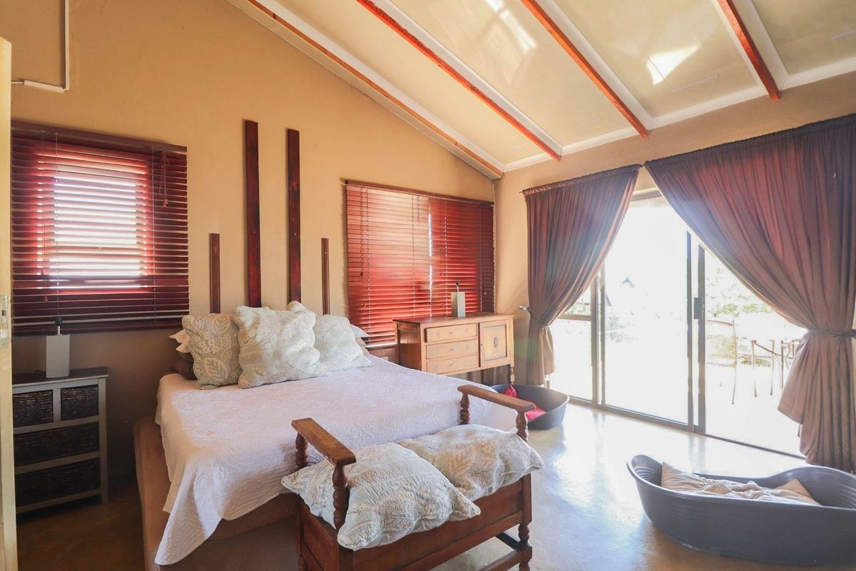 Spacious bedroom featuring vaulted ceilings with exposed timber beams, large windows with timber blinds, and sliding glass doors leading to an outdoor area.