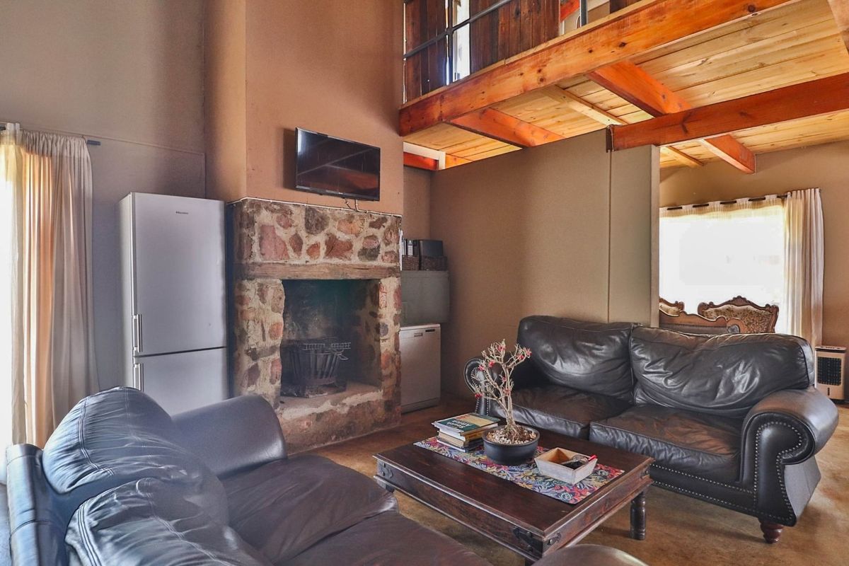 A rustic living area featuring a stone-clad fireplace, exposed timber ceiling beams, and a mezzanine level overlooking the main space.
