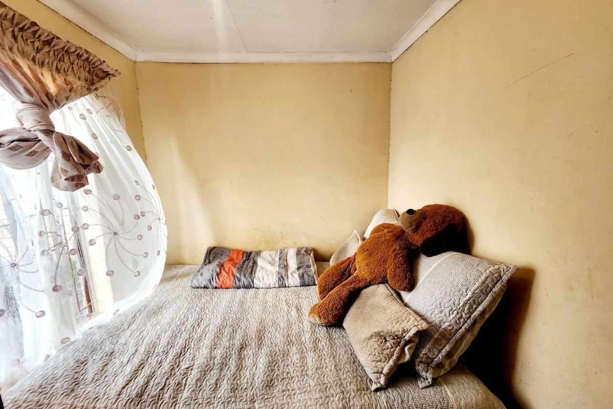 A compact bedroom featuring plain walls and a window with curtains, requiring cosmetic updates to improve the overall aesthetic and finish.