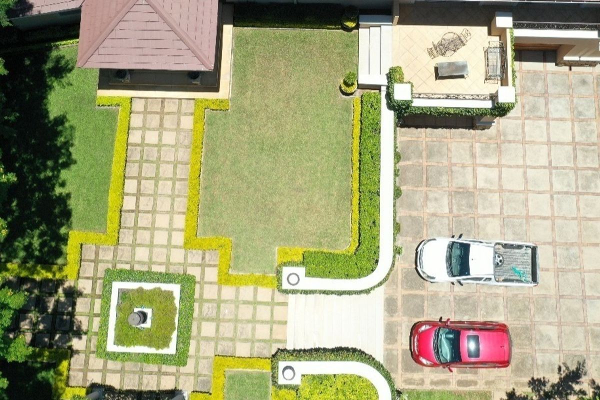Aerial view of the property grounds featuring a large paved driveway, manicured garden with hedging, and a covered patio area.