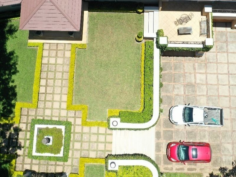 Aerial view of the property grounds featuring a large paved driveway, manicured garden with hedging, and a covered patio area.