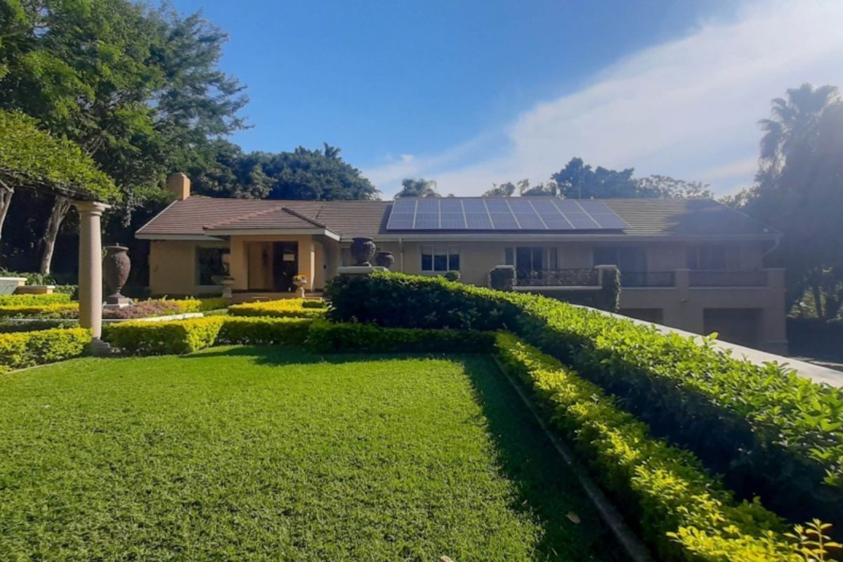 A well-maintained rear exterior view of the house featuring a landscaped garden, stone columns, a pergola, and roof-mounted solar panels.