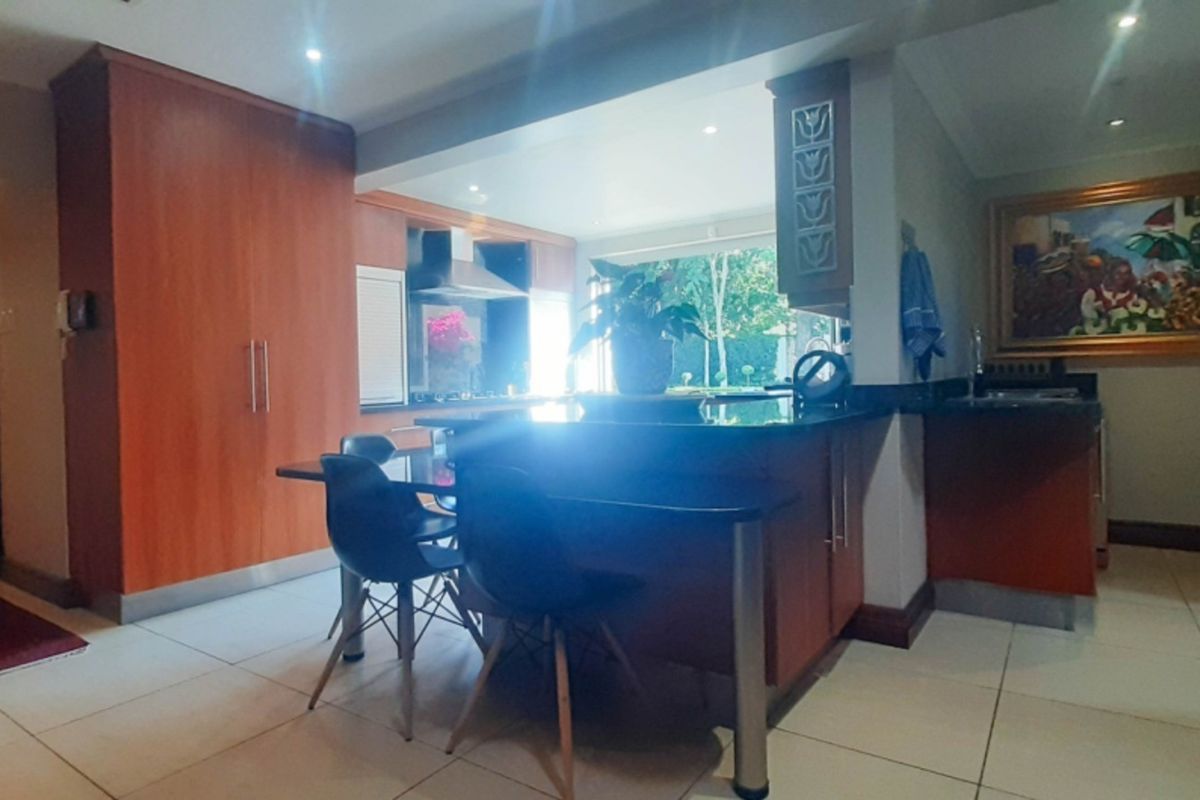 A functional kitchen featuring warm wood-toned cabinetry, dark granite countertops, and tiled flooring, with an integrated breakfast bar and recessed lighting.