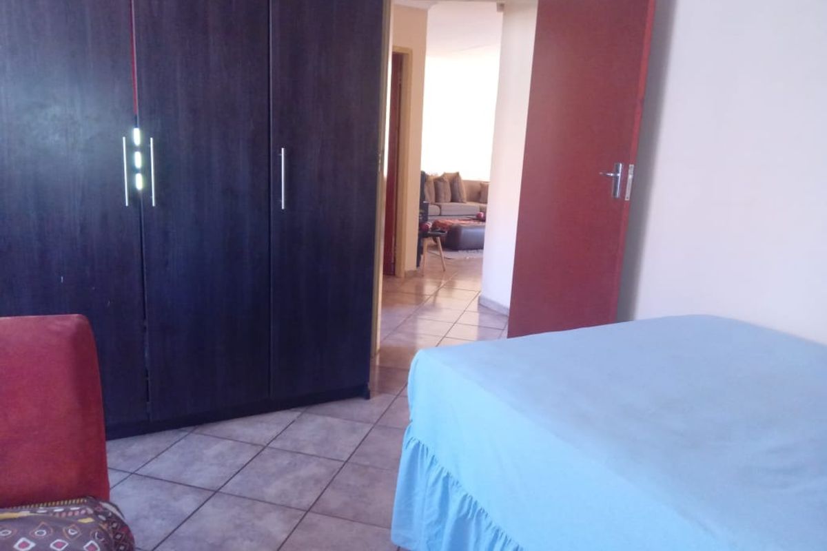 A bedroom featuring built-in dark wood cabinetry and tiled flooring, with a view through the doorway into an adjacent living area.