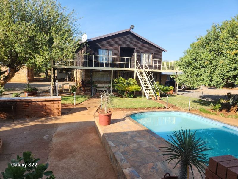 A two-story farm dwelling featuring a raised balcony, external staircase, and a private swimming pool set within a landscaped garden area.