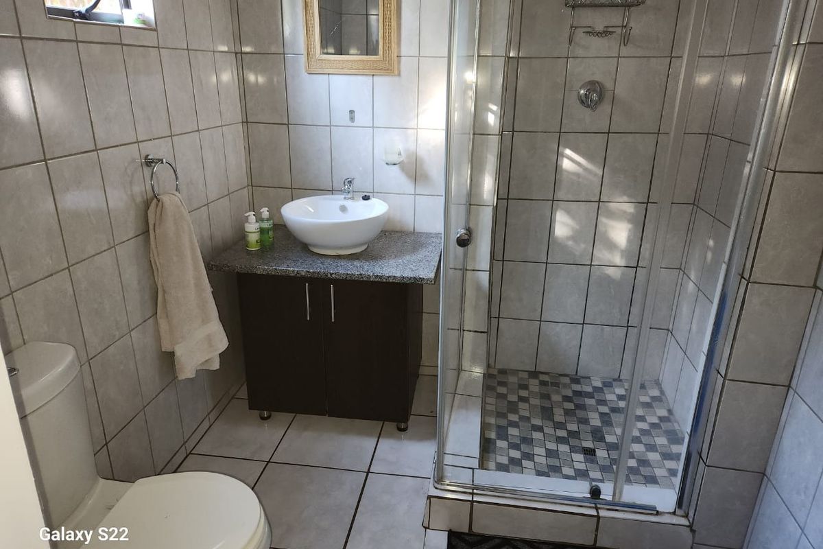 A functional bathroom featuring a glass-enclosed shower, a modern vessel sink vanity, and full-height wall tiling.