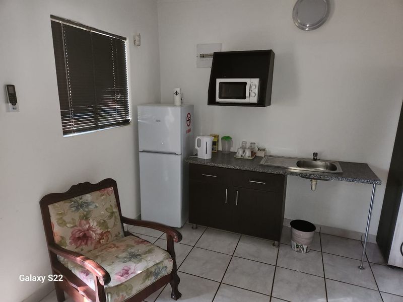 A compact kitchenette area featuring a single base cabinet, stainless steel sink, and wall-mounted microwave shelf with tiled flooring.
