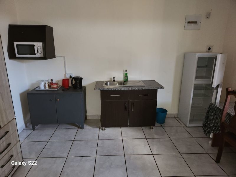 A functional kitchenette area featuring a stainless steel sink, dark cabinetry, tiled flooring, and a wall-mounted microwave shelf.