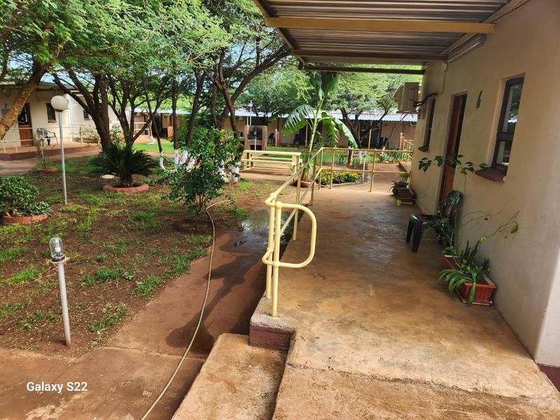 A covered patio area overlooking a landscaped garden with mature trees, featuring a metal railing and direct access to the building exterior.