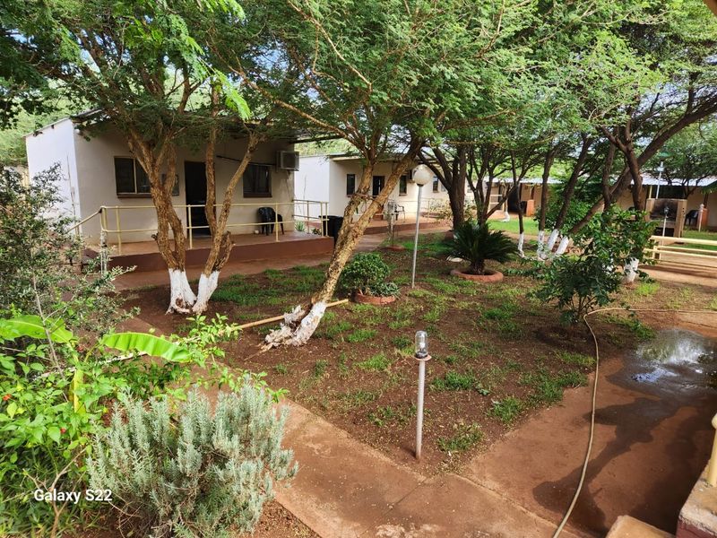 A view of the farm property featuring multiple detached units with covered porches set within a landscaped garden area with mature trees.