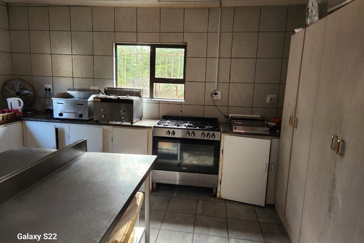 A functional farm-style kitchen featuring stainless steel prep surfaces, a gas stove with oven, and tiled walls, requiring cosmetic updates.
