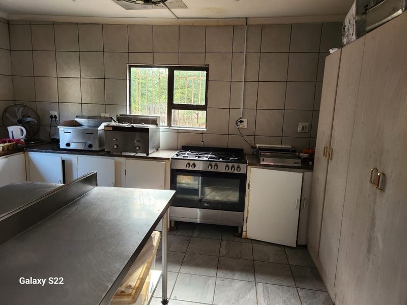 A functional farm-style kitchen featuring stainless steel prep surfaces, a gas stove with oven, and tiled walls, requiring cosmetic updates.