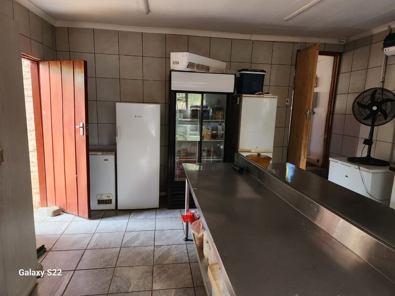 A functional utility or scullery area featuring stainless steel prep surfaces, tiled walls and flooring, and multiple refrigeration units.