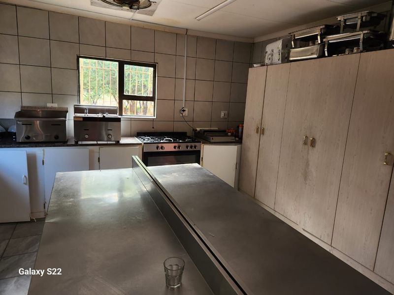 Commercial-style kitchen featuring stainless steel prep counters, built-in oven and hob, and extensive storage cabinetry with tiled wall finishes.