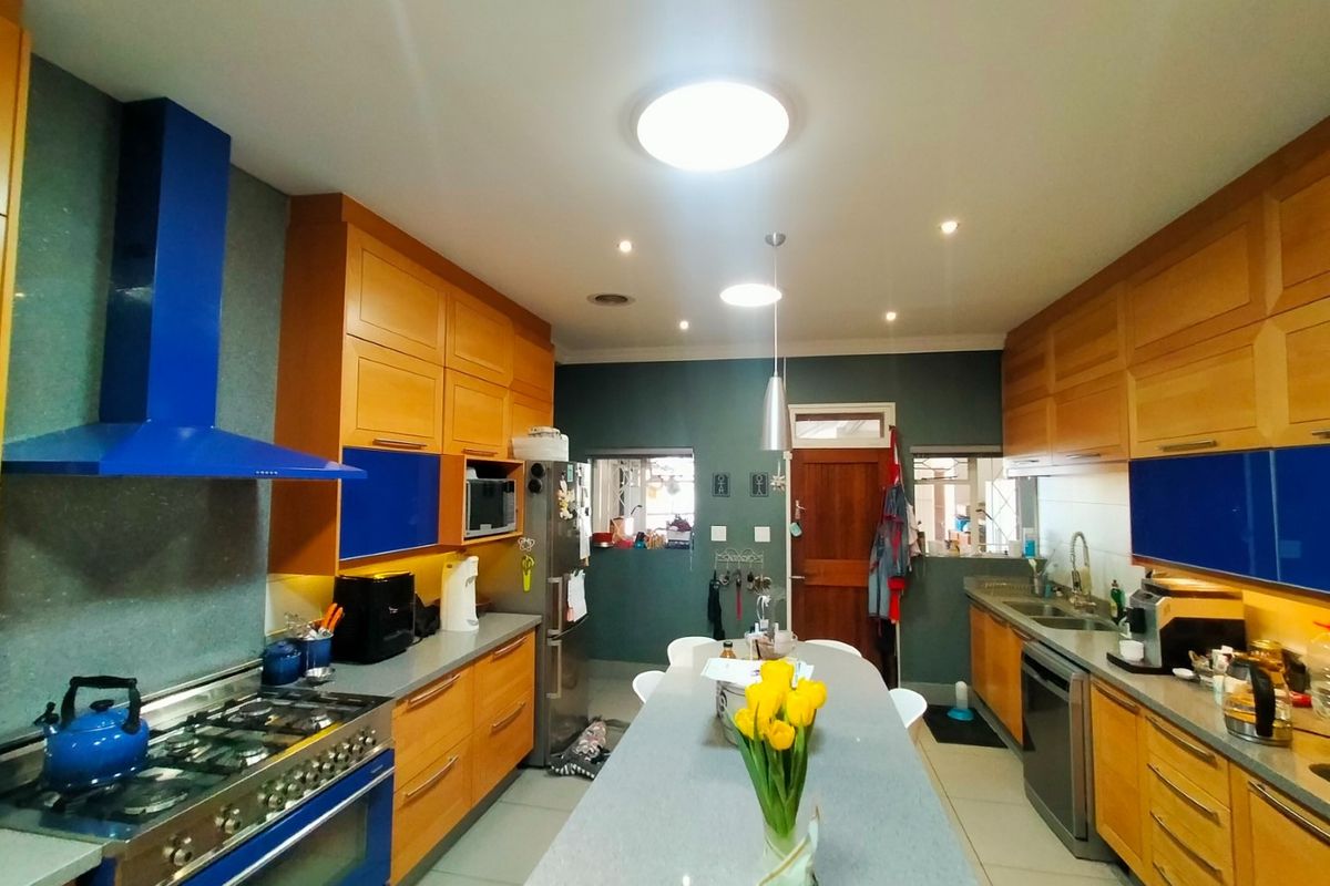 A spacious kitchen featuring wooden cabinetry, a central island with stone countertop, a gas stove with a blue extractor hood, and tiled flooring.