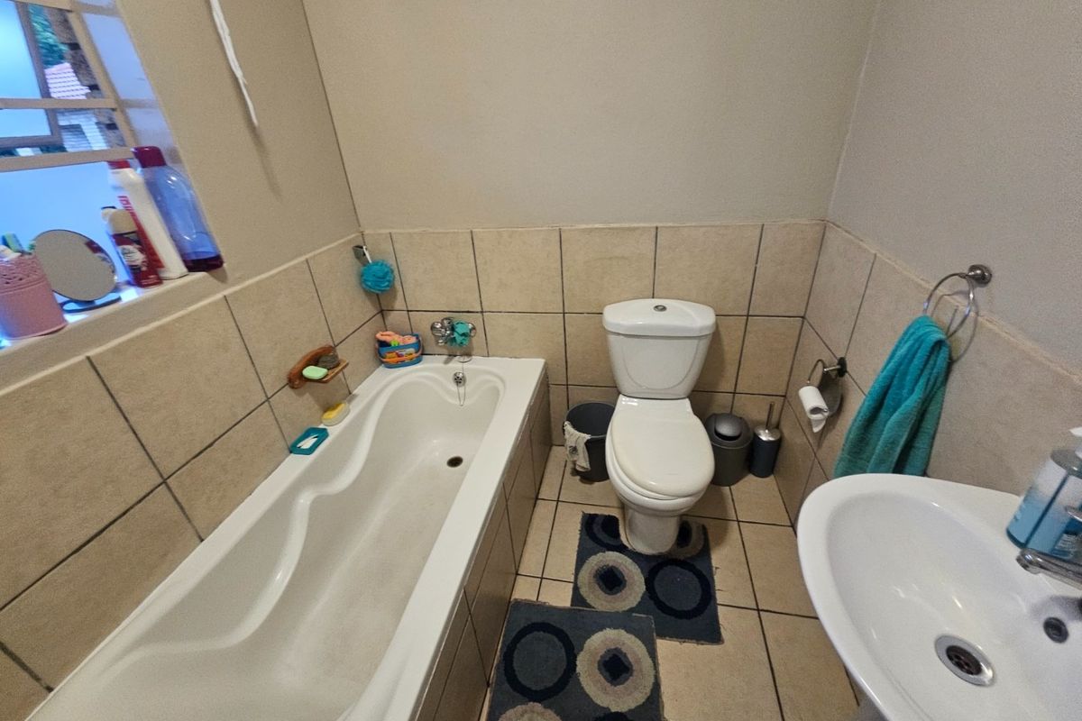 A functional bathroom featuring a standard bathtub, pedestal basin, and toilet with neutral wall and floor tiling.