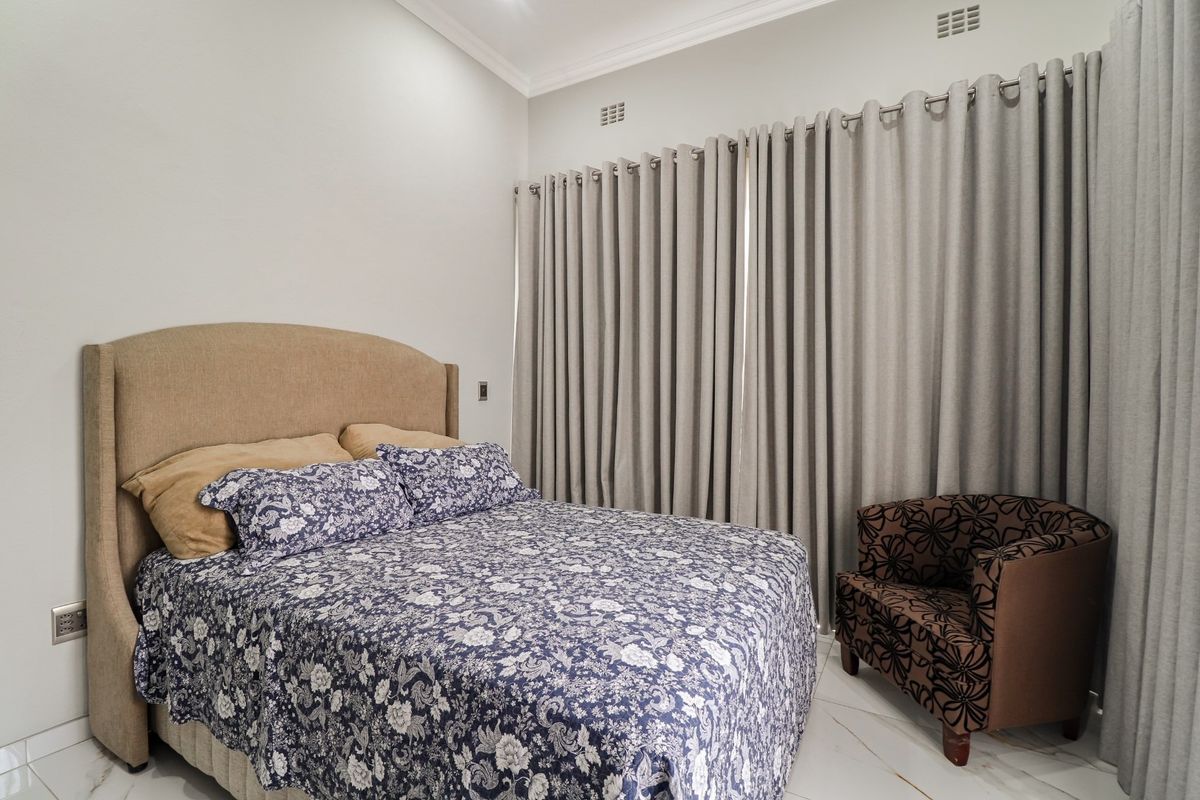 A well-maintained bedroom featuring neutral wall tones, tiled flooring, and floor-to-ceiling curtains providing ample natural light control.