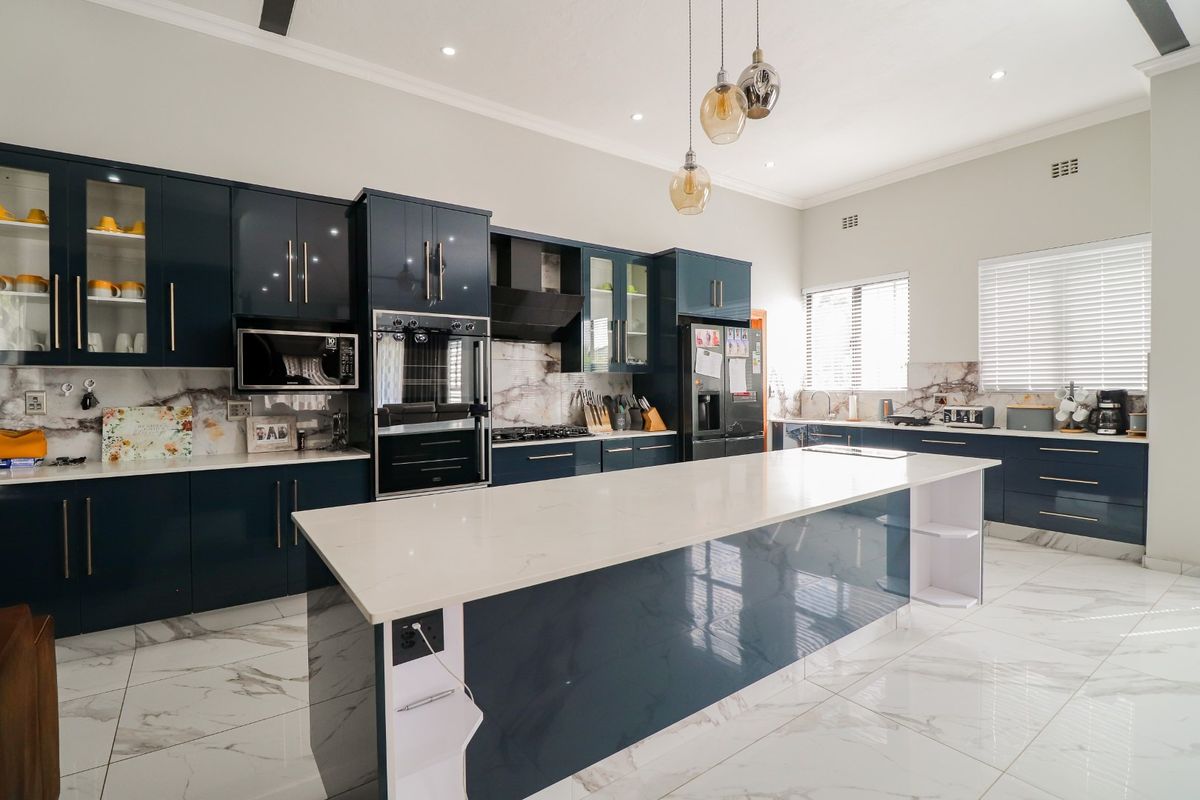 Modern kitchen featuring dark blue cabinetry, white stone countertops, a large central island, marble-look floor tiles, and integrated stainless steel appliances.