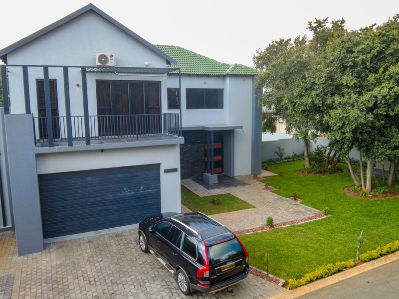 A modern two-story residential property featuring a paved driveway, double garage, balcony, and a well-maintained garden area.