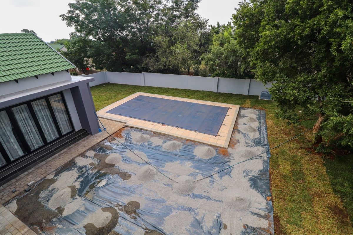 Aerial view of a backyard featuring a swimming pool with a cover, adjacent to a house with a green tiled roof and ongoing landscaping work.