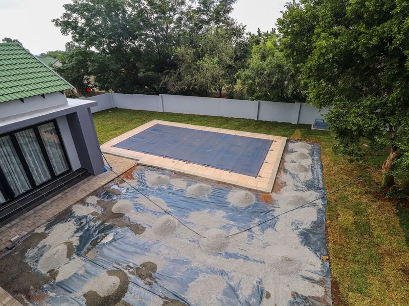Aerial view of a backyard featuring a swimming pool with a cover, adjacent to a house with a green tiled roof and ongoing landscaping work.