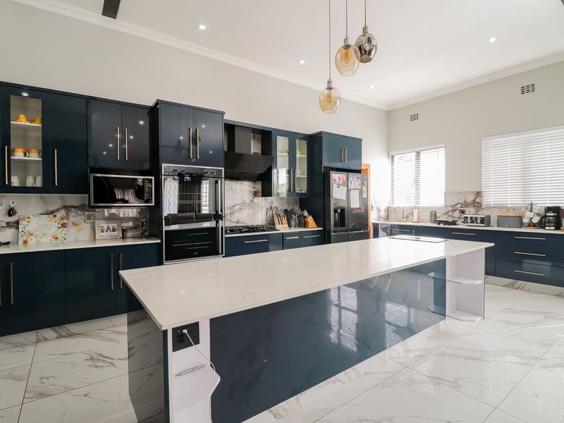 Modern kitchen featuring dark blue cabinetry, white stone countertops, a large central island, marble-look floor tiles, and integrated stainless steel appliances.