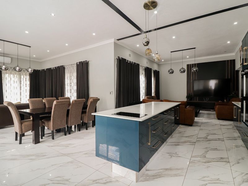 Modern open-plan living area featuring a sleek kitchen island with integrated cooktop, marble-look tiled flooring, and contemporary pendant lighting throughout the space.