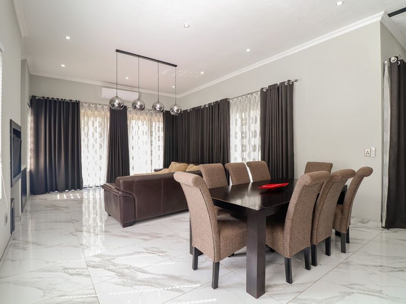 Spacious open-plan living and dining area featuring polished marble-look floor tiles, recessed downlighting, and large windows with floor-to-ceiling curtains.