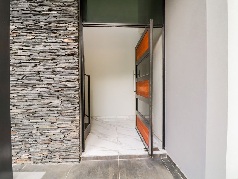Modern entrance featuring a stacked stone feature wall, large format marble-look floor tiles, and a contemporary timber and glass pivot door.
