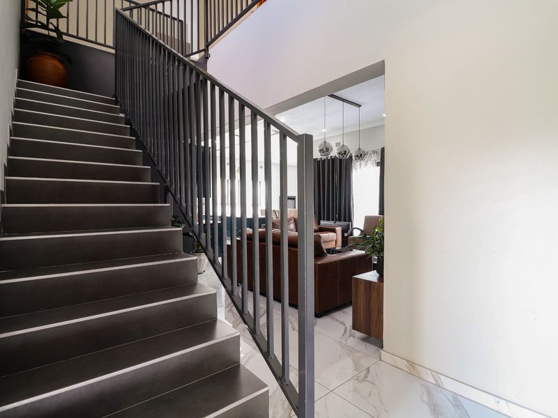 A modern staircase with dark tiled steps and a sleek black metal balustrade, leading to an open-plan living area with marble-look floor tiles.