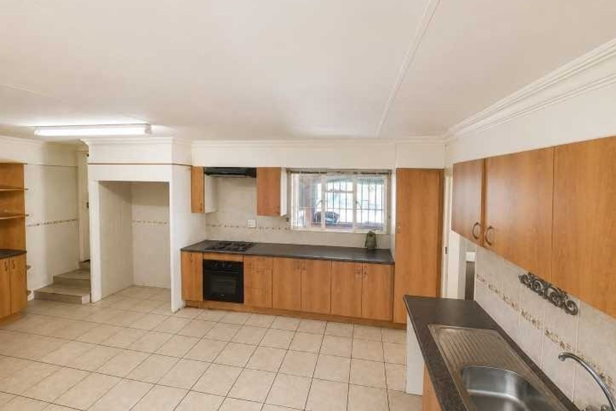 Spacious kitchen featuring built-in wooden cabinetry, integrated oven and hob, tiled flooring, and ample counter space, offering a functional layout ready for modernization.