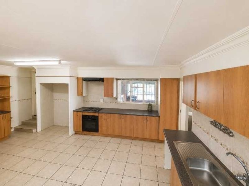 Spacious kitchen featuring built-in wooden cabinetry, integrated oven and hob, tiled flooring, and ample counter space, offering a functional layout ready for modernization.