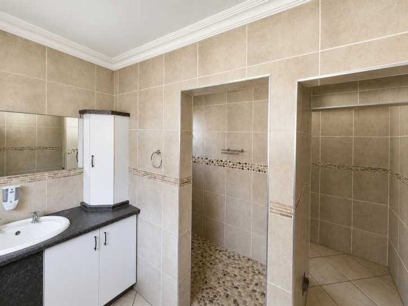 A clean bathroom featuring a vanity with basin, tiled walls, and a walk-in shower with a pebble floor finish.