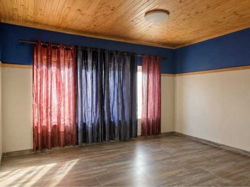 A spacious, empty bedroom featuring a natural timber ceiling, tiled flooring, and two-tone wall finishes.