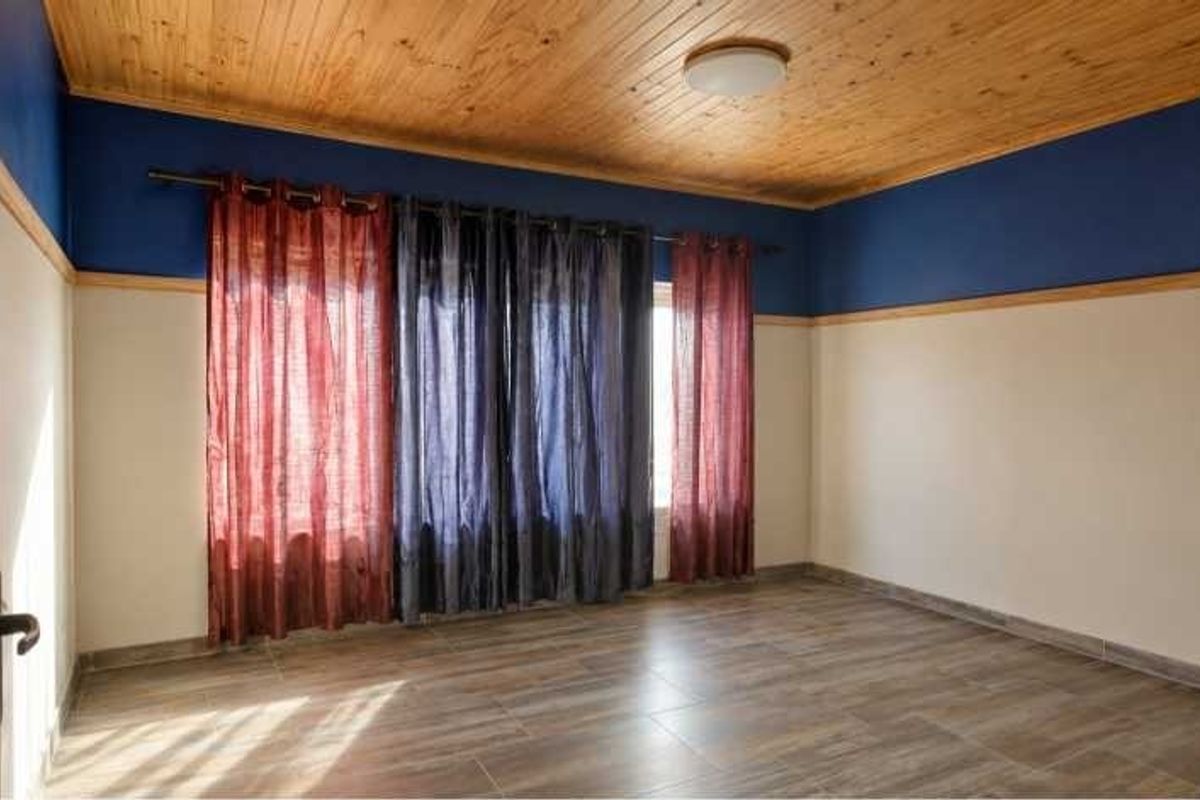 A spacious, empty bedroom featuring a natural timber ceiling, tiled flooring, and two-tone wall finishes.