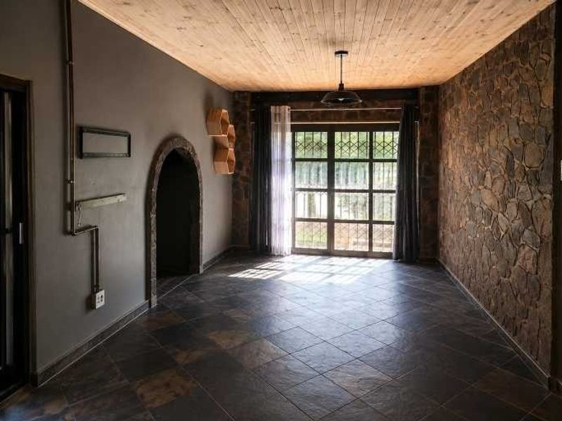 Spacious living area featuring a rustic stone accent wall, timber-clad ceiling, dark tiled flooring, and an arched doorway leading to adjacent space.