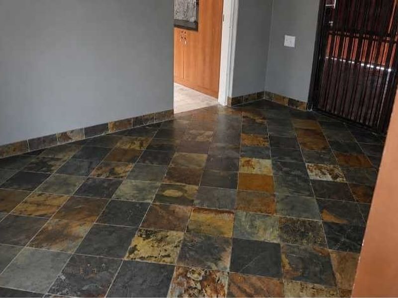 A vacant hallway featuring durable slate tile flooring and a secure metal gate, providing access to adjacent living areas.