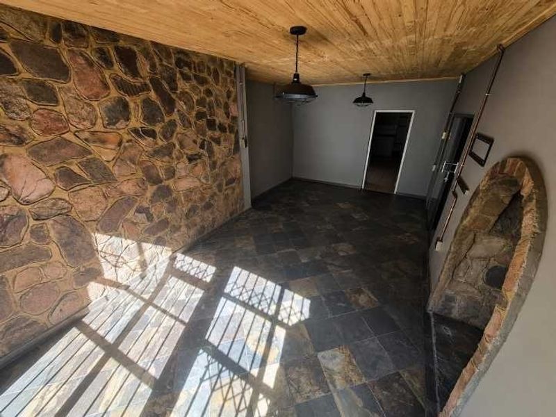 A covered patio area featuring rustic stone wall cladding, slate tile flooring, and a timber ceiling, providing a unique outdoor entertainment space.