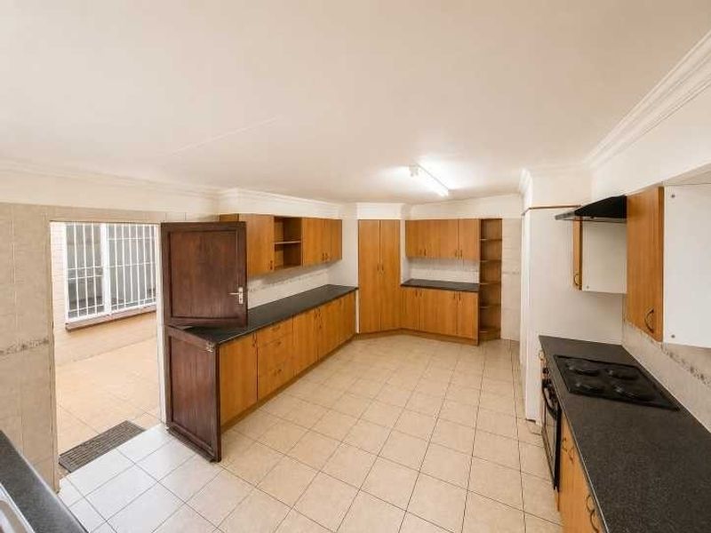 Spacious kitchen featuring extensive built-in cabinetry, dark laminate countertops, electric hob, and direct access to an outdoor area through a security gate.