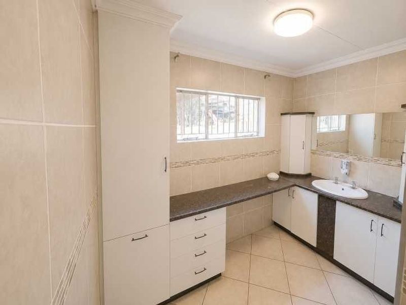 A clean, functional bathroom featuring tiled walls and floors, built-in vanity cabinetry with ample storage, and a large wall-mounted mirror.
