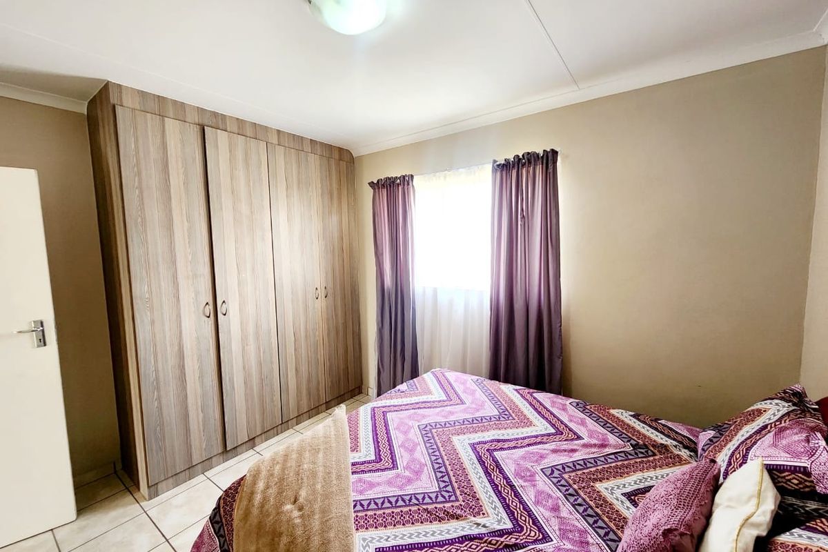 A bedroom featuring built-in wooden wardrobes, tiled flooring, and a ceiling-mounted light fixture.