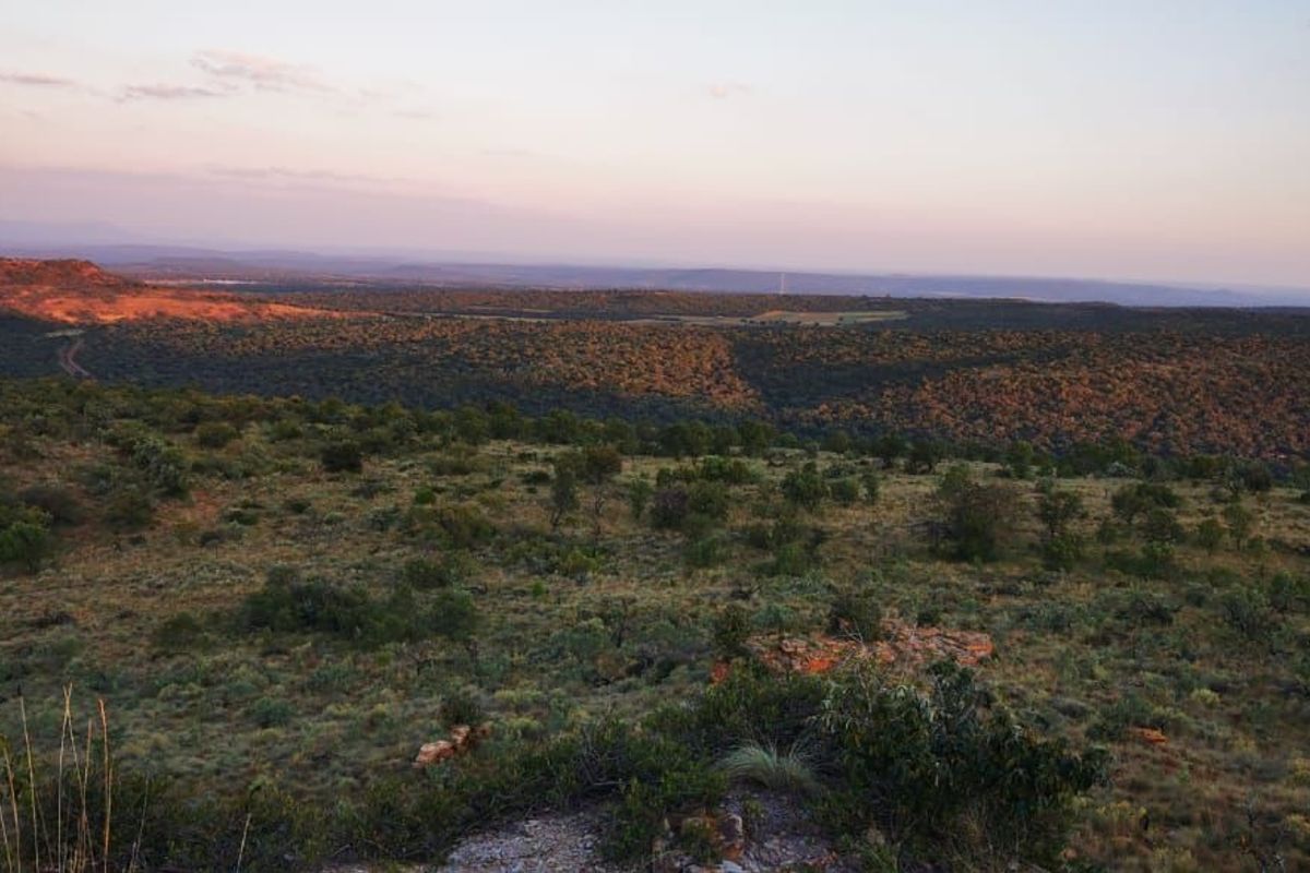 A scenic, elevated view overlooking the expansive natural landscape and rolling hills of the vacant residential property at sunset.