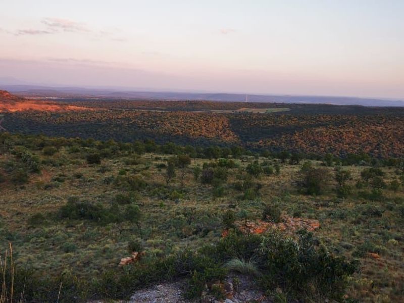 A scenic, elevated view overlooking the expansive natural landscape and rolling hills of the vacant residential property at sunset.