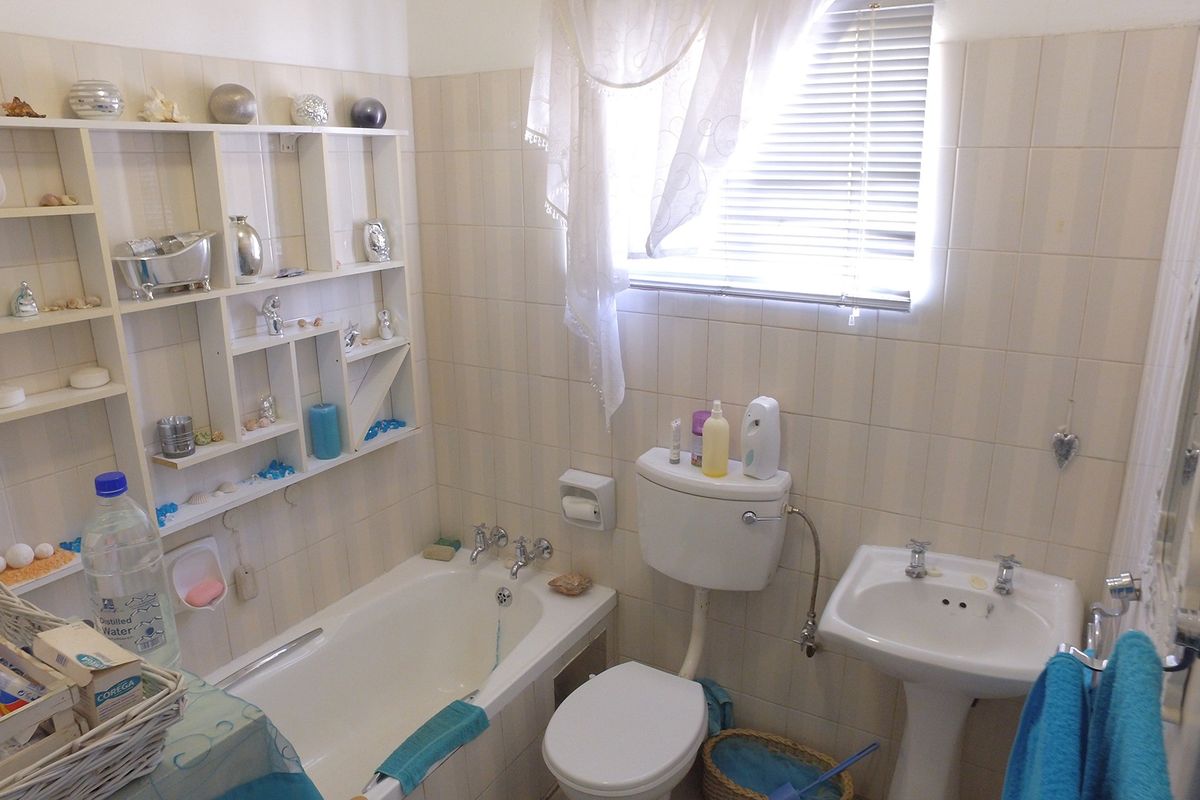 A functional bathroom featuring a standard bathtub, pedestal basin, and toilet, finished with neutral wall tiles and built-in shelving.