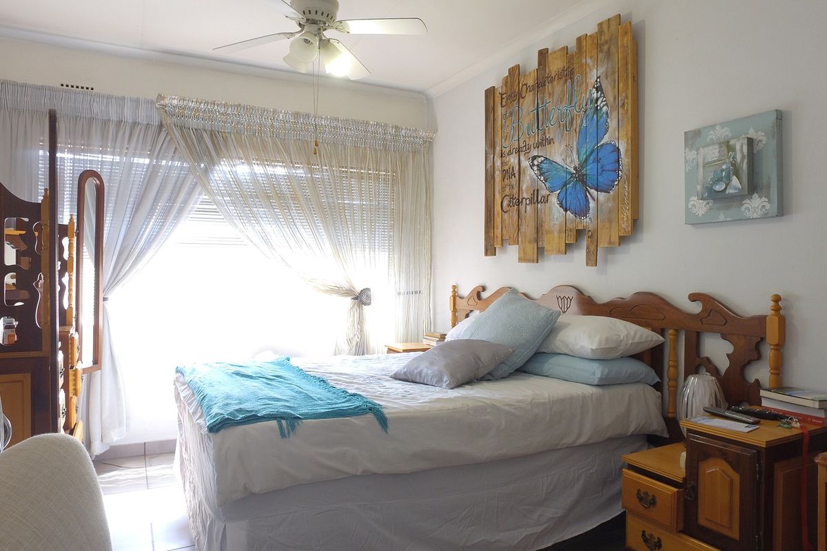 A well-lit bedroom featuring a ceiling fan and large window with curtains, providing a comfortable and functional living space.